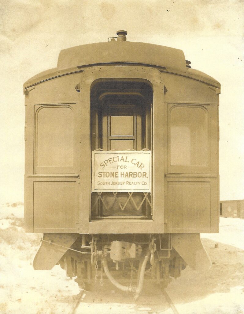 Vintage sepia photograph showing the rear of a railroad parlor car on tracks, with a sign reading "SPECIAL CAR FOR STONE HARBOR, South Jersey Realty Co." hung in the open rear doorway.
