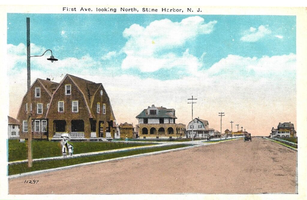 Color picture postcard titled "First Ave. looking North, Stone Harbor, N. J." showing a wide avenue with a large shingled cottage on the left, several homes along the street, electric poles, and a woman with a parasol and a child on the sidewalk at lower left.