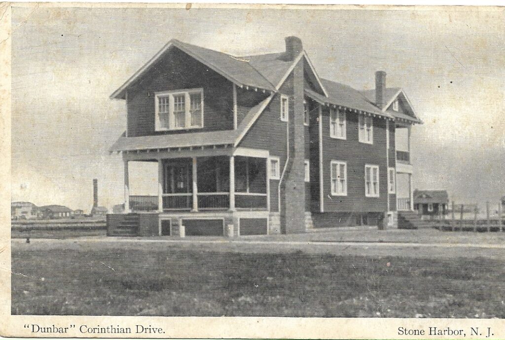 Vintage postcard of the "Dunbar," a two-story shingled building with a wrap-around screened porch, two chimneys, and gabled roofline, captioned "'Dunbar' Corinthian Drive. Stone Harbor, N. J." A water tower and other structures are faintly visible in the background.