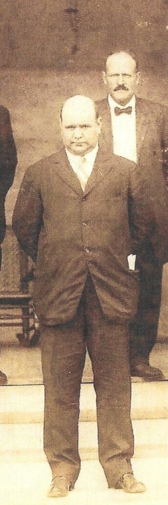 Cropped sepia photograph of Stone Harbor's first mayor Howard Risley in a dark three-piece suit standing facing the camera, with a second man partially visible behind him.