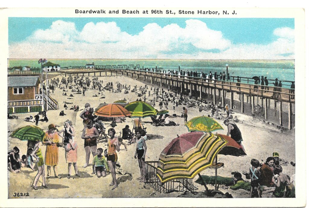 A colorized vintage postcard titled “Boardwalk and Beach at 96th St., Stone Harbor, N.J.” showing a crowded beach scene with colorful umbrellas in the foreground and the elevated wooden boardwalk extending along the right side toward a pier in the distance.