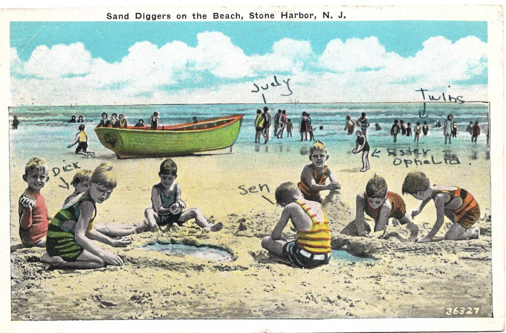 A colorized vintage postcard titled “Sand Diggers on the Beach, Stone Harbor, N.J.” showing a group of children in bathing suits digging in the wet sand, with handwritten names identifying several of them. A green rowboat sits on the sand behind them, and beachgoers wade in the shallow water in the background.
